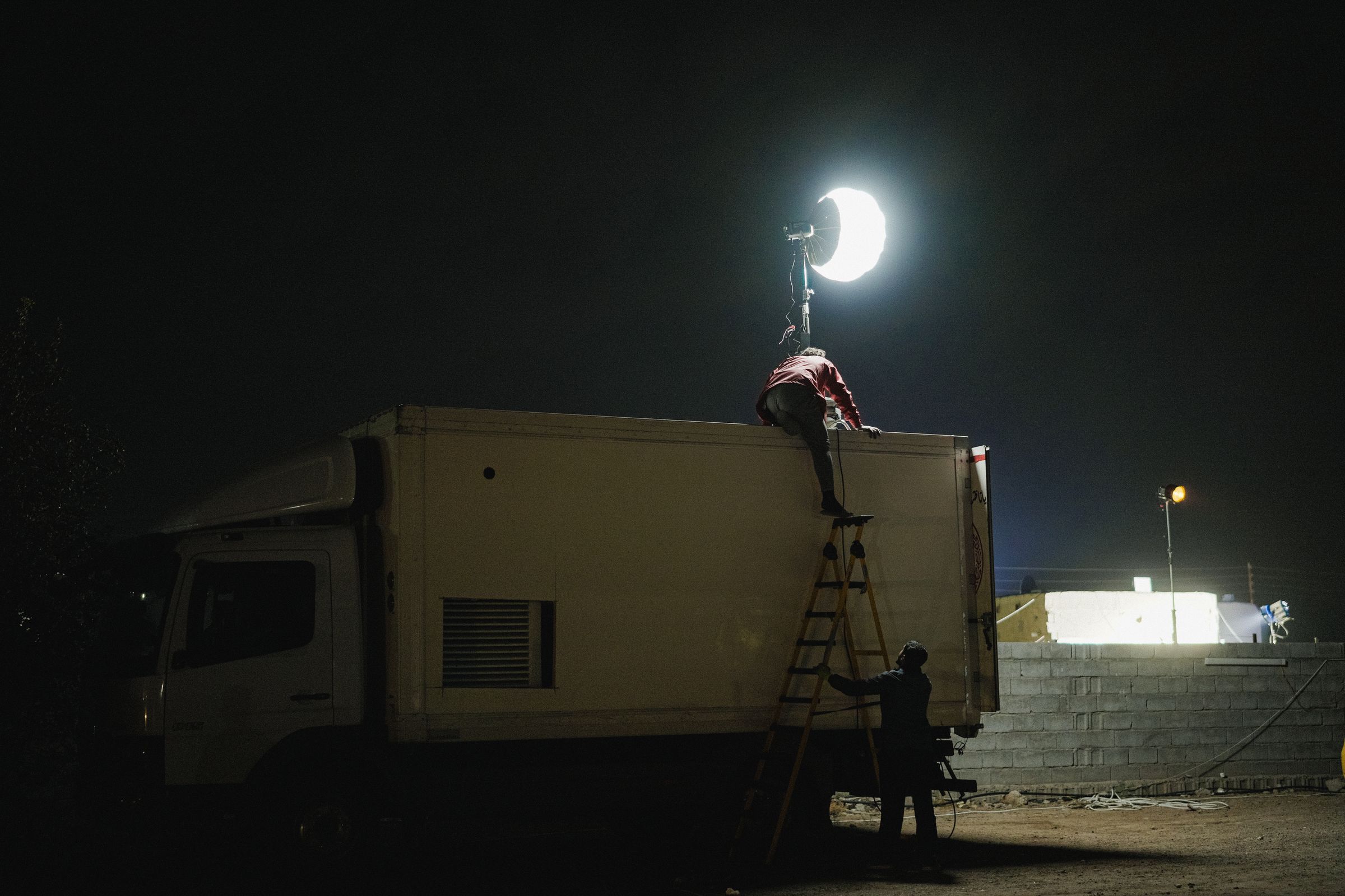 A film crew setting up lights on a truck at night.