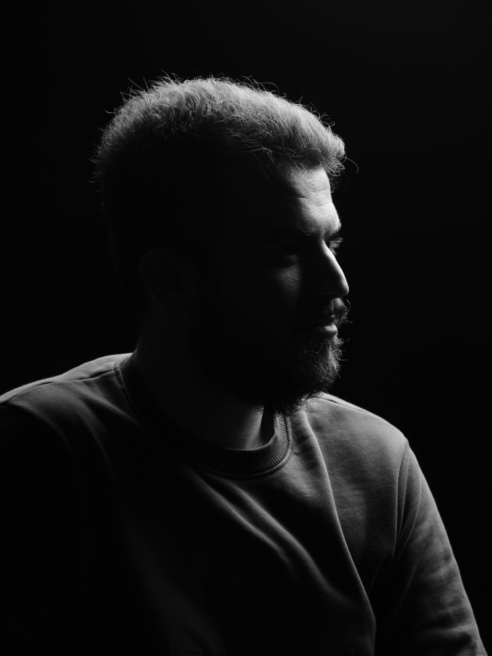 A side-lit portrait of a bearded man in monochrome.