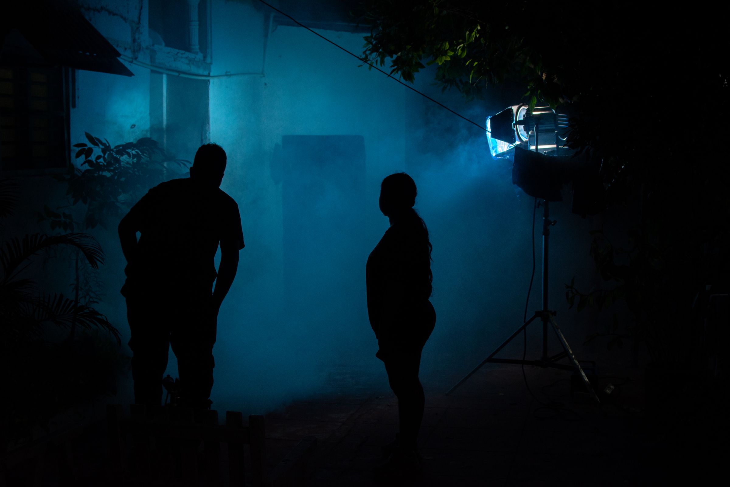 Two silhouettes lit against blue mist at night.